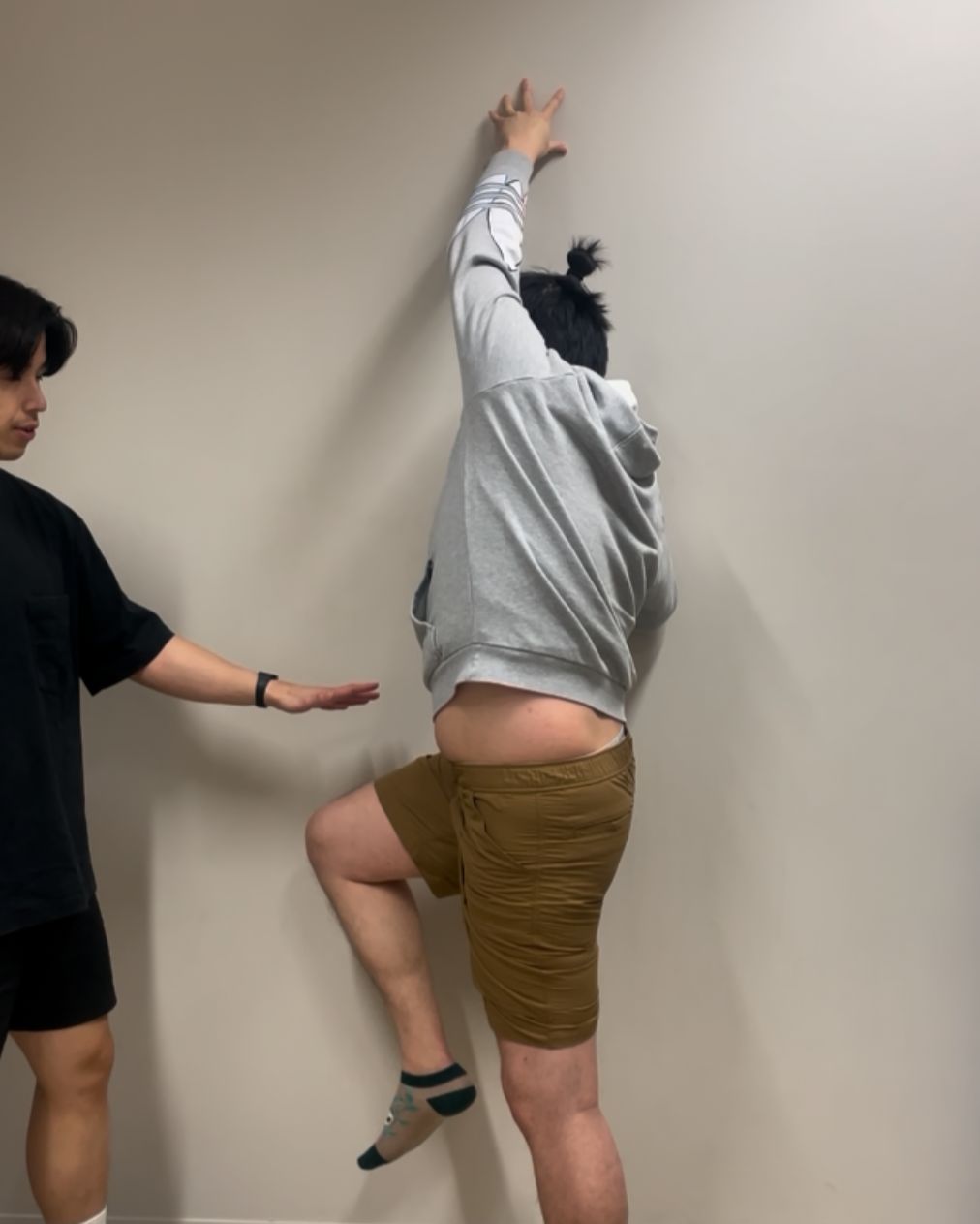 Fan guiding a patient through a movement assessment against the clinic wall